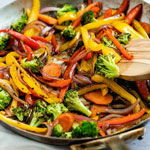 A cook is making fried vegetables in a pan.