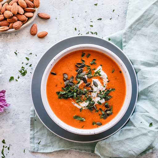 A bowl of tomato soup topped with a sprinkle of thyme leaves and a side bowl of almonds.